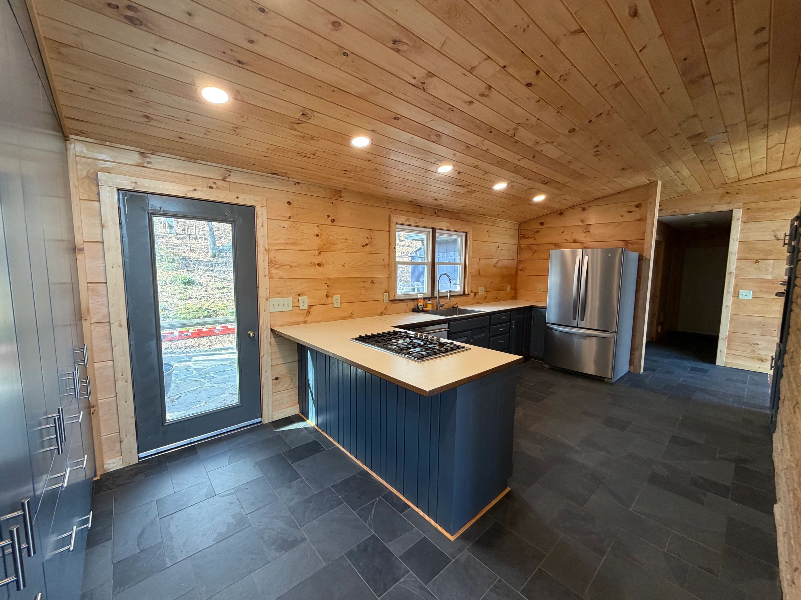 Modern kitchen remodel with navy cabinets, slate tile floor and stainless fridge